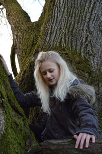 Portrait of beautiful young woman against tree trunk