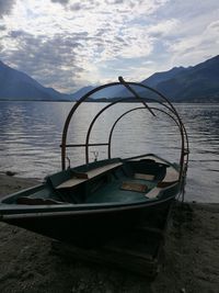 Boat moored on shore by lake against sky