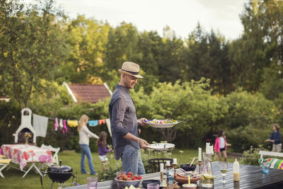 Man carrying plates by dining table in back yard during garden party