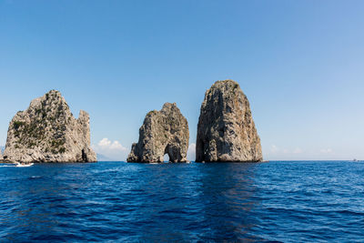 Rocks in sea against clear blue sky