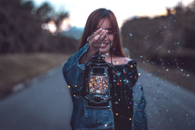 Portrait of woman holding camera while standing outdoors