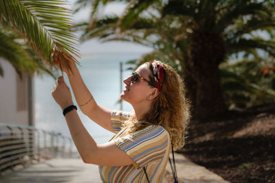 Side view of woman wearing sunglasses touching leaves