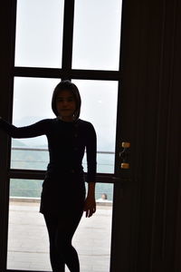 Portrait of young woman standing against window in room