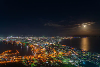 High angle view of illuminated city by sea against sky at night