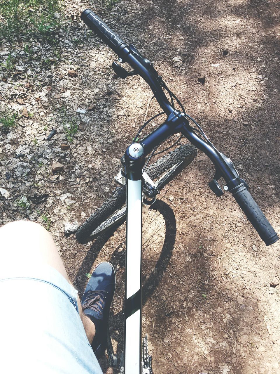 high angle view, personal perspective, street, shadow, part of, sunlight, road, day, outdoors, unrecognizable person, bicycle, cropped, transportation, leisure activity, asphalt, lifestyles, low section