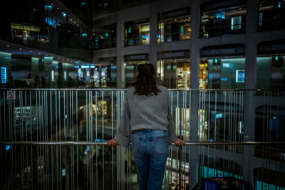 Rear view of woman standing by railing in city at night
