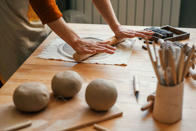 Artisan woman in lighted pottery studio, rolling clay for modelling