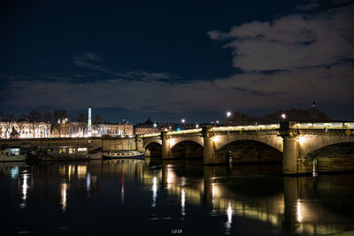 Illuminated bridge over river against sky in city at night