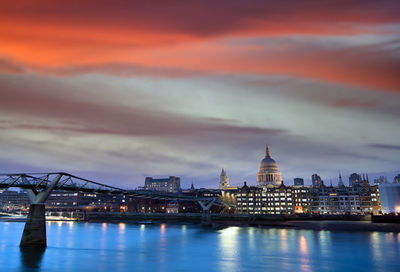 Illuminated city at waterfront against cloudy sky