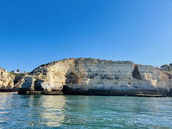 Rock formations in sea against clear blue sky