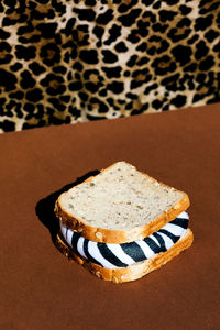 Crop anonymous person in shirt with leopard print sitting at brown table with sandwich with zebra filling in light room