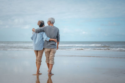 Rear view of couple walking on shore at beach