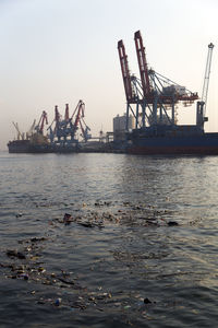 Low angle view of cranes by sea against clear sky