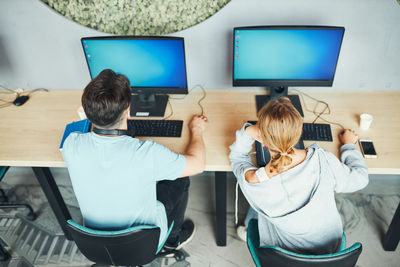 Rear view of woman using digital tablet while sitting on table