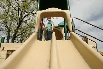 Low angle portrait of boy standing on slide at playground