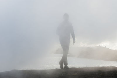 Rear view of silhouette man standing by sea in foggy weather