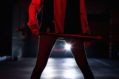 Crop legs of faceless woman in jeans and black boots with massive sole holding bat with car headlights on background