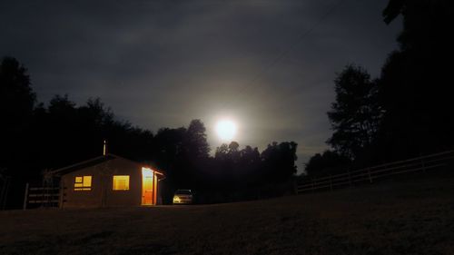 Illuminated house by trees against sky