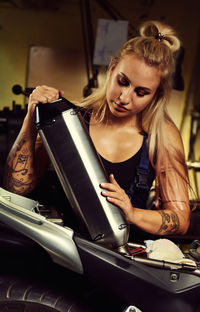 Young woman holding exhaust pipe in motorcycle while standing at workshop