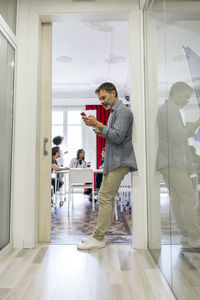 Male entrepreneur using smart phone while leaning on doorway in office