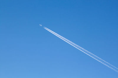 Low angle view of vapor trails against clear blue sky