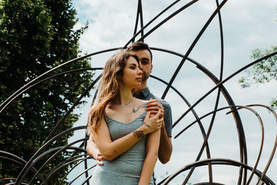 Low angle view of young woman standing by railing against sky