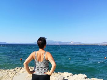 Rear view of woman standing on beach against clear blue sky