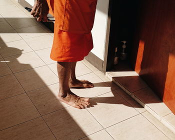 Low section of monk standing by door on tiled floor