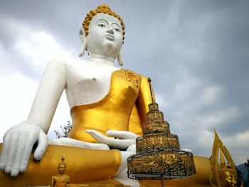 Low angle view of large buddha statue against cloudy sky