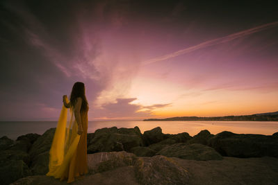 Woman in a yellow dress and cape observing a magnificent sunrise on the french basque coast iii