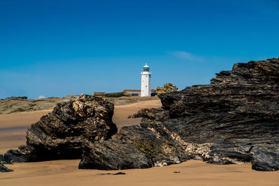 Lighthouse on sand dune against clear blue sky