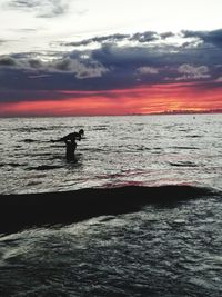 Silhouette man in sea against sky during sunset