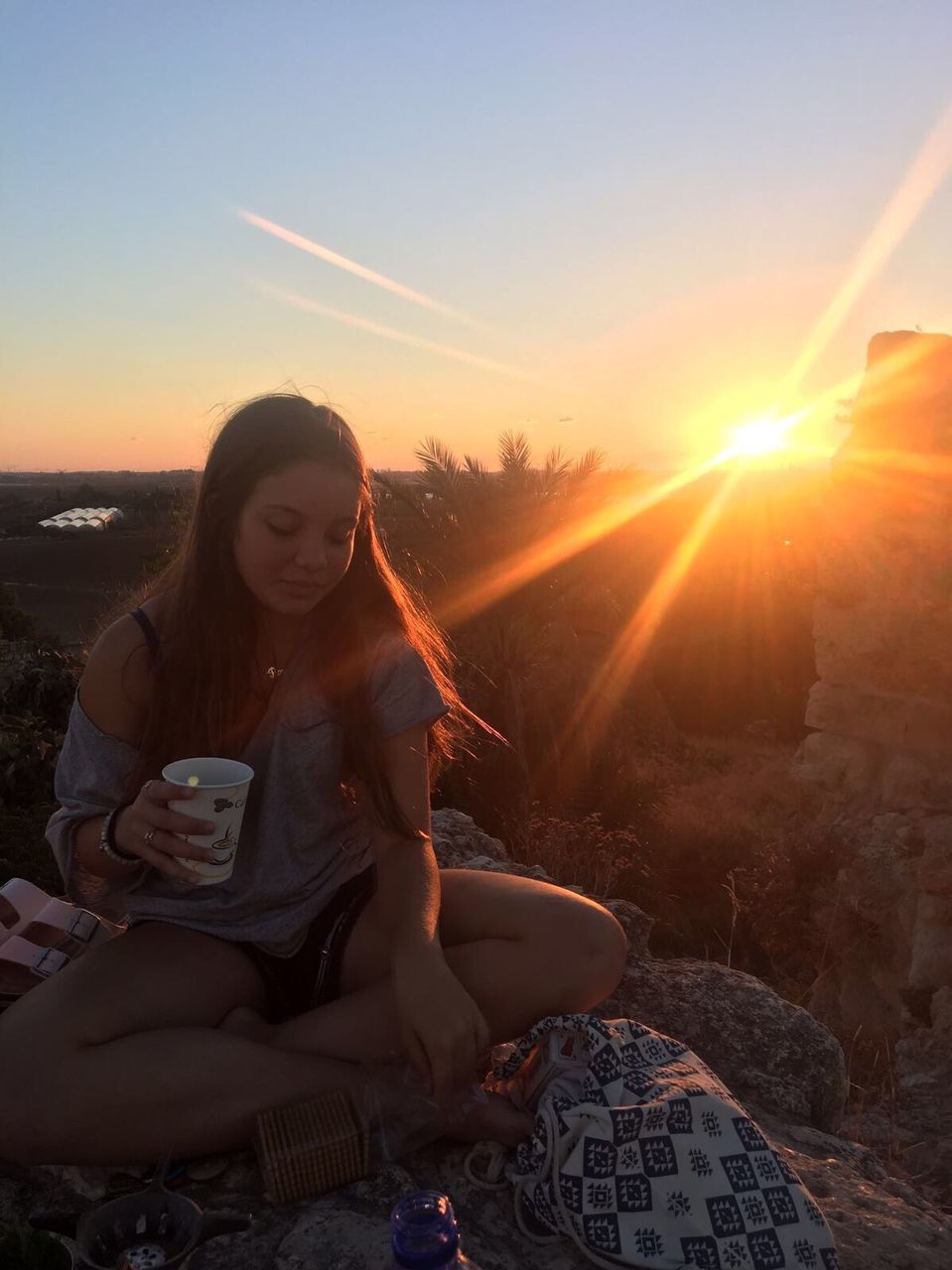 sunset, sun, sunlight, real people, sunbeam, sitting, lens flare, one person, wireless technology, full length, leisure activity, young adult, young women, lifestyles, holding, communication, nature, outdoors, mobile phone, technology, sky, beauty in nature, day, people