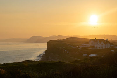 Scenic view of sea and cliffs against orange sky