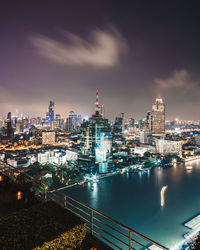 Illuminated buildings by river against sky in city at night