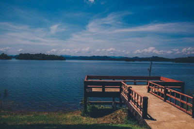 Empty bench by lake against sky