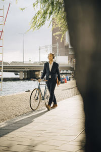 Businessman walking with bicycle on footpath in city during sunny day