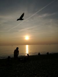 Silhouette men flying over sea against sky during sunset