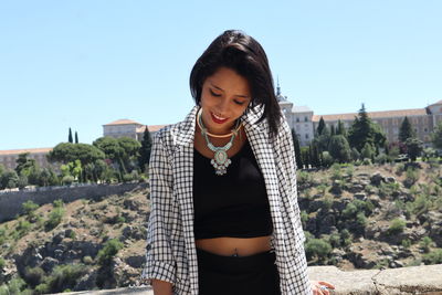 Smiling young woman standing against clear sky