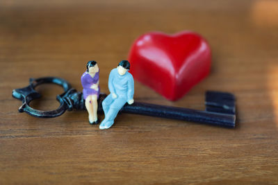 High angle view of figurines sitting on key with heart shape at wooden table