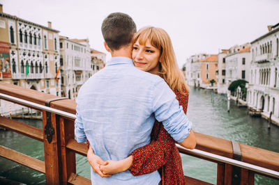 Woman embracing boyfriend on bridge over river in city