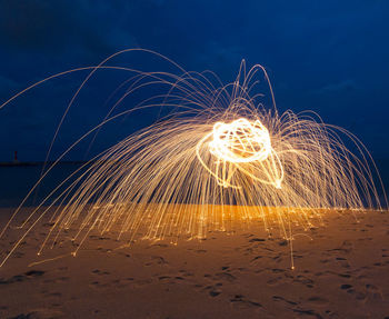 Illuminated light painting over sand at beach against sky during night