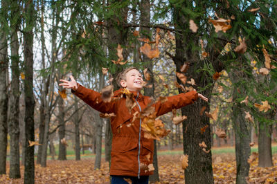 The boy tossed autumn yellow leaves and looks up
