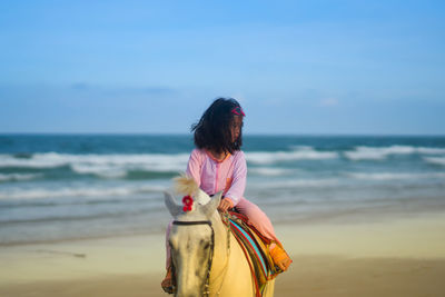 Rear view of girl riding on horse ft at beach against sky