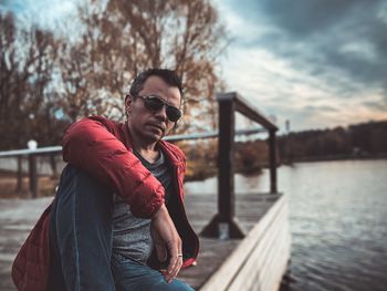 Man wearing sunglasses standing by railing against lake