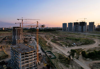 Aerial view of construction site by buildings against sky during sunset