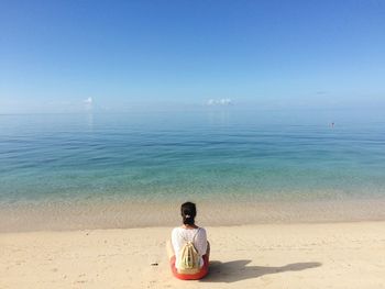 Rear view of woman relaxing on sand at beach against blue sky