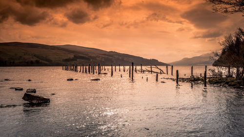 Wooden posts in sea against sky during sunset