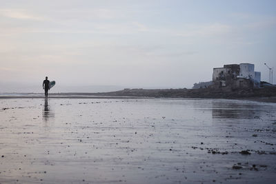 Rear view of man standing at beach against sky