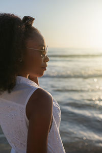 Midsection of young woman looking at sea shore against sky